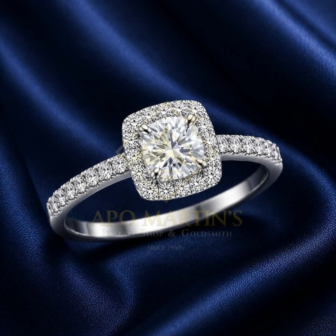 A square halo engagement ring with a cushion-cut center diamond and pavé-set band, displayed on a dark blue satin fabric background. A watermark for 'APO MARTIN'S' is visible across the lower center.
