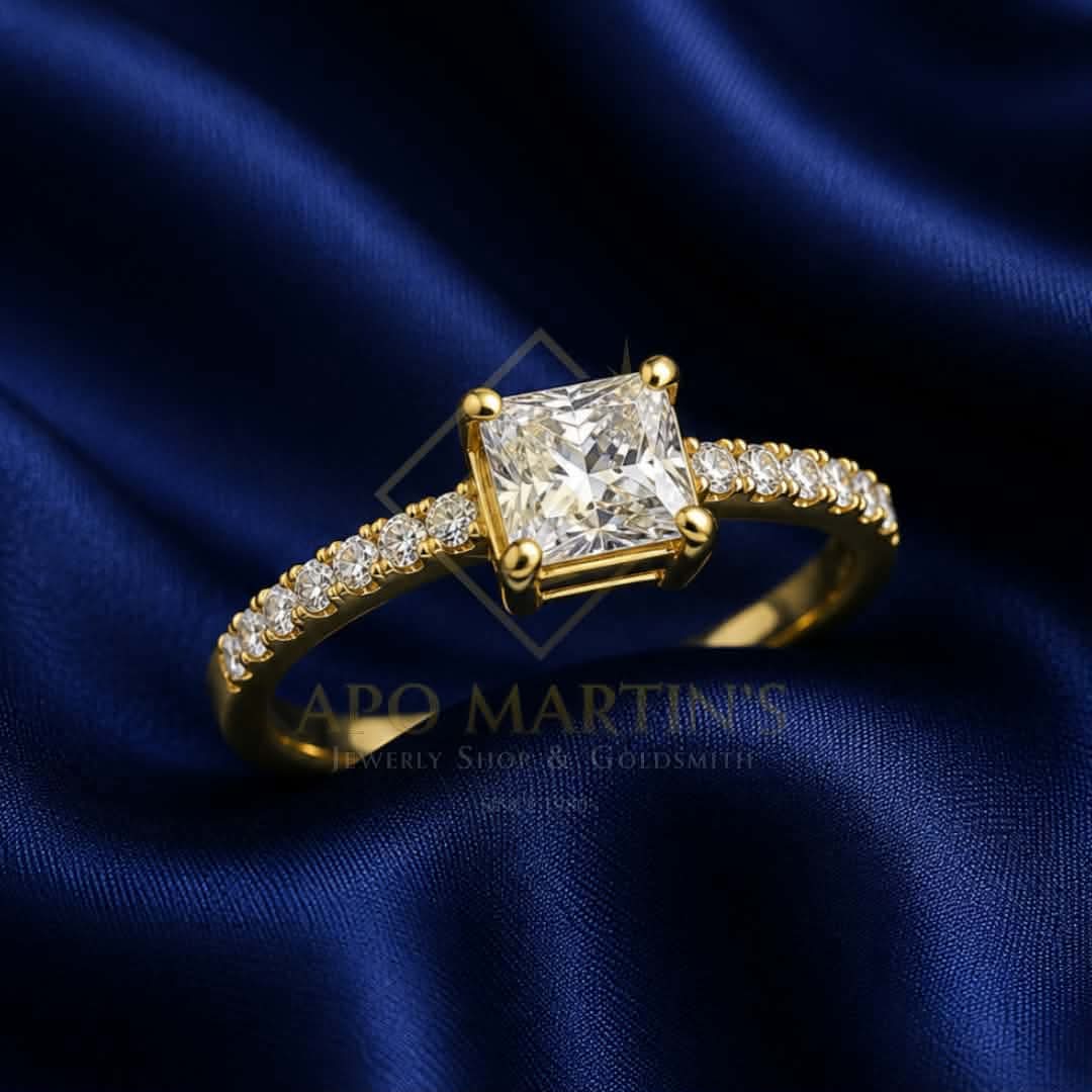 A yellow gold ring featuring a princess-cut diamond center stone and a pavé band set with small round diamonds, displayed on a dark blue satin fabric background. A watermark for 'Apo Martin's Jewelry Shop & Goldsmith' is visible across the lower center.
