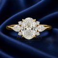 An oval-cut diamond engagement ring with marquise and round diamond accents on a yellow gold band, displayed on a dark blue satin fabric background. A watermark for 'Apollo Goldsmith's Jewelry Shop & Goldsmith' is visible across the center.