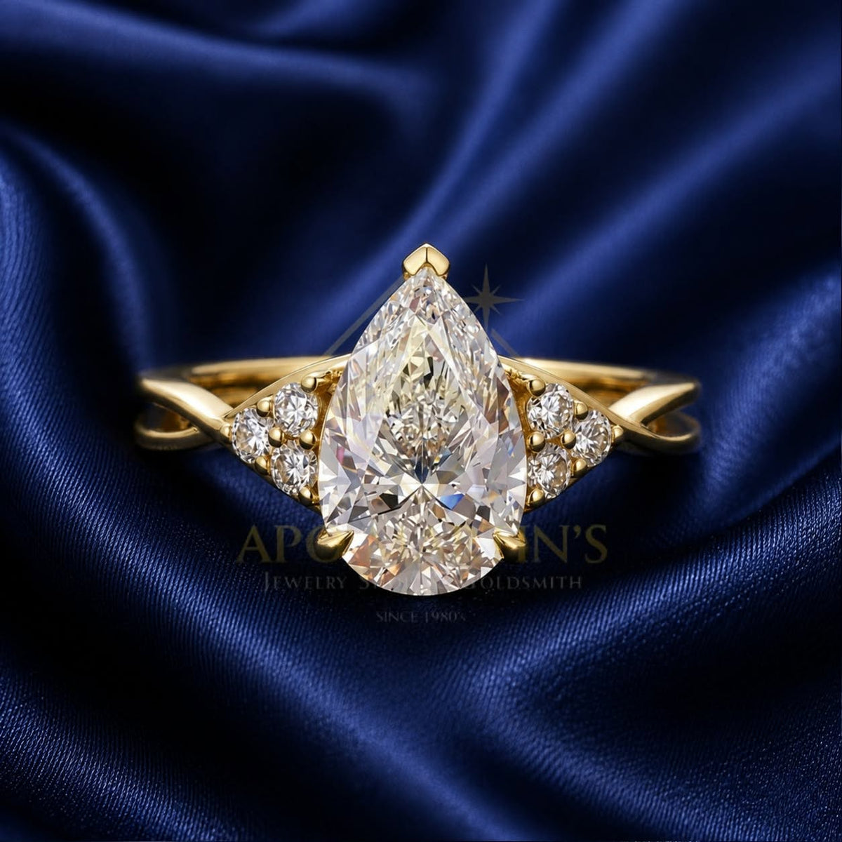 A yellow gold ring featuring a large pear-cut center diamond flanked by smaller diamonds on the band, displayed on a dark blue satin fabric background.